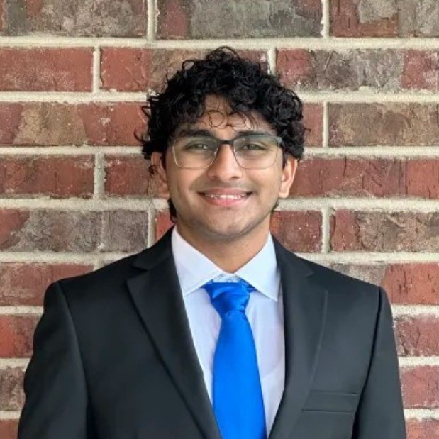 Vedant Soni wearing a blue tie, standing in front of a brick wall